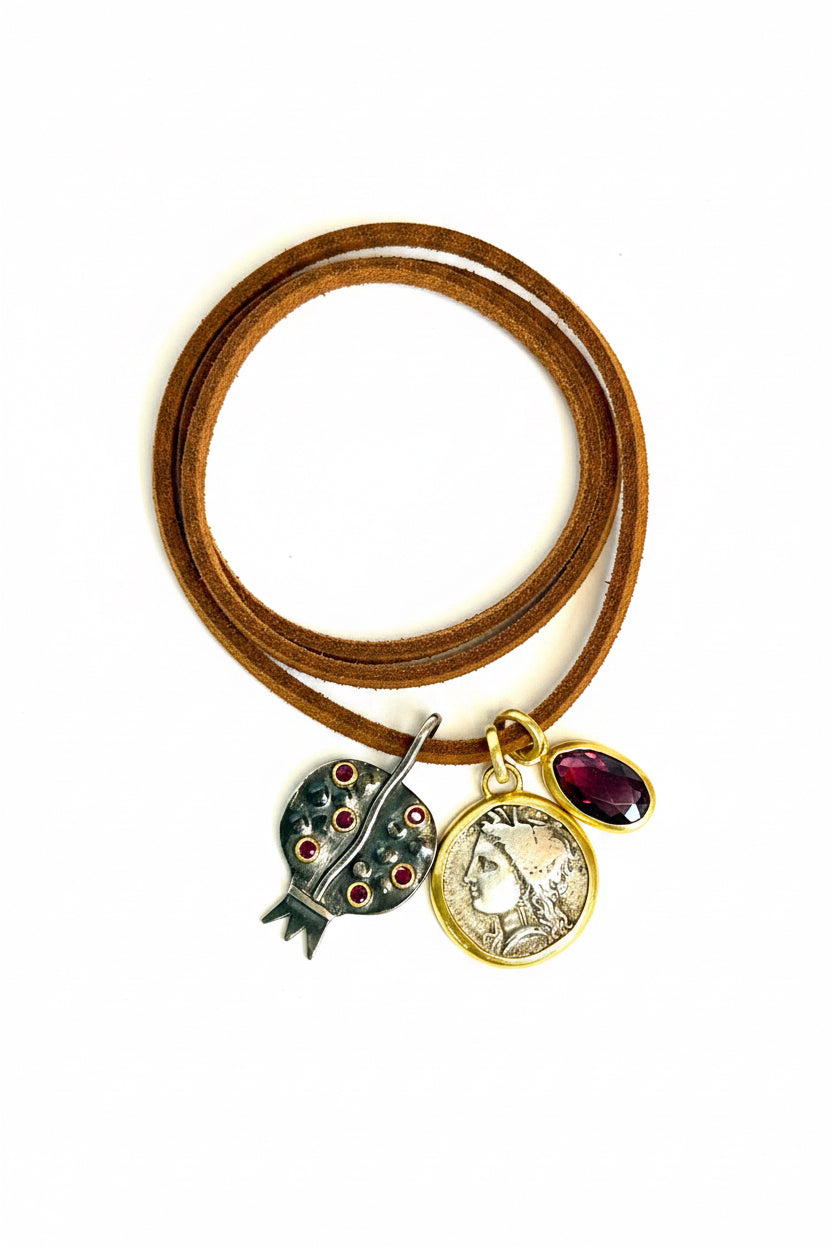 Gold necklace with pomegranate pendant, a coin pendant, and a ruby pendant on a white background