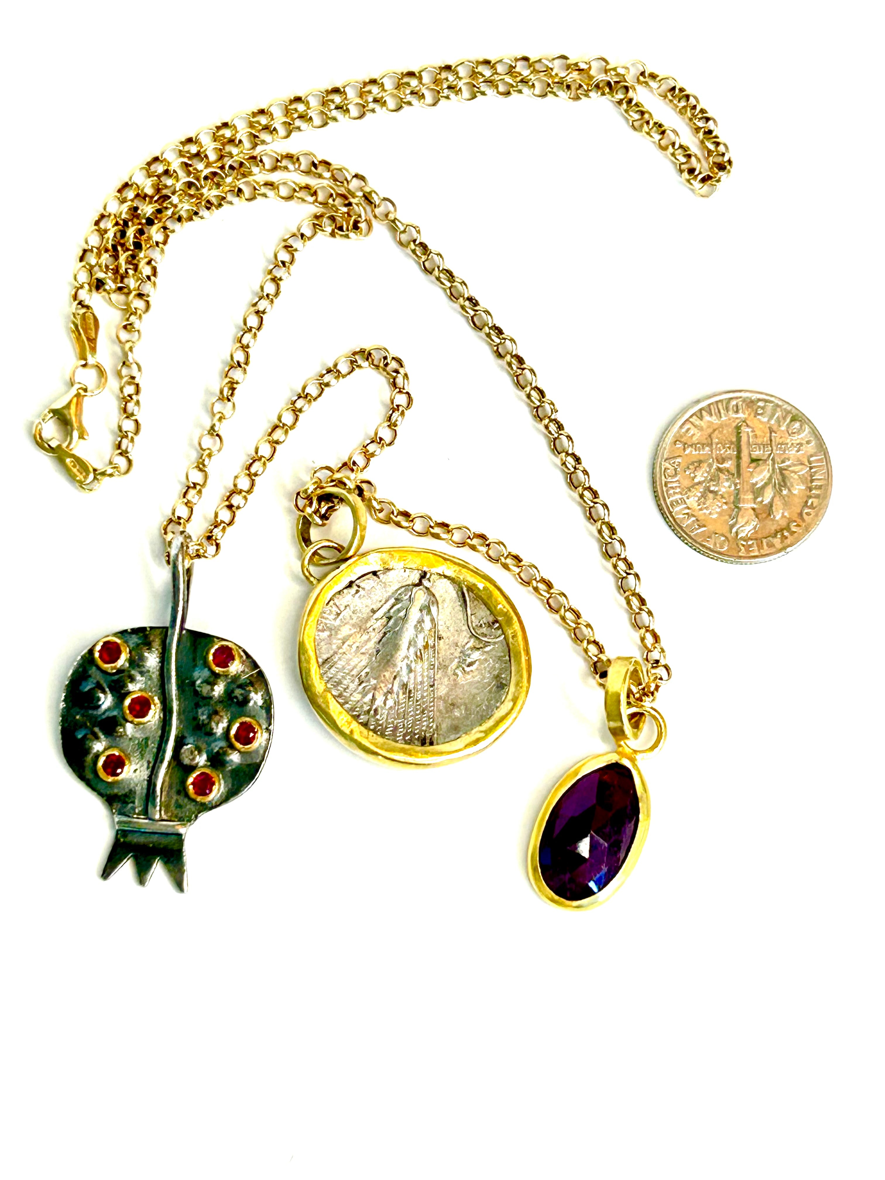Gold necklace with various pendants including a coin, a gemstone dotted pomegranate pendant, and a ruby pendant on a white background