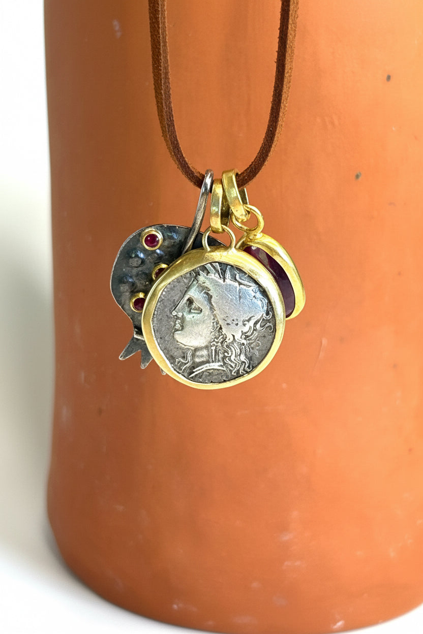 Gold chain necklace with a coin charm, a pomegranate pendant, and a ruby pendant on a terracotta surface