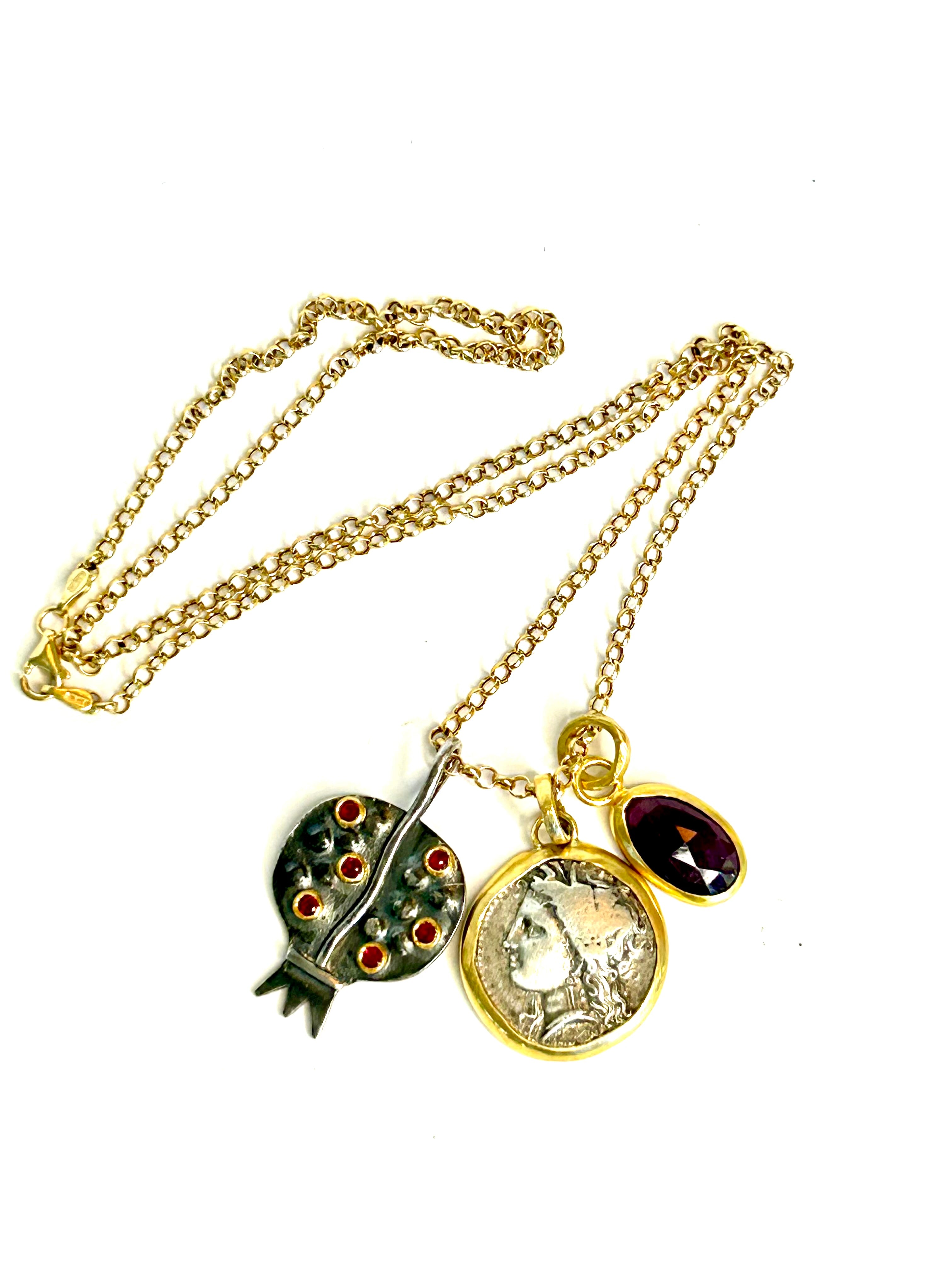 Gold necklace with pomegranate pendant, a coin pendant, and a ruby pendant on a white background